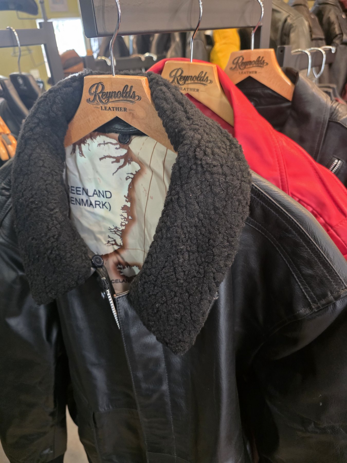 Black sherpa-collar leather jacket on a Reynolds Leather hanger with map lining — try on in the shop